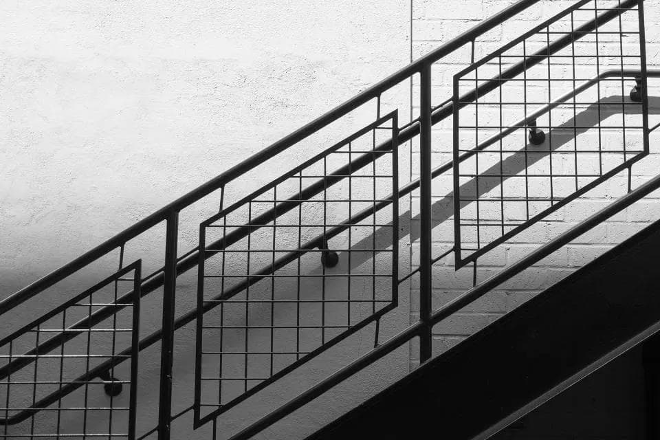 Black metal stair railing with a grid pattern against a white wall
