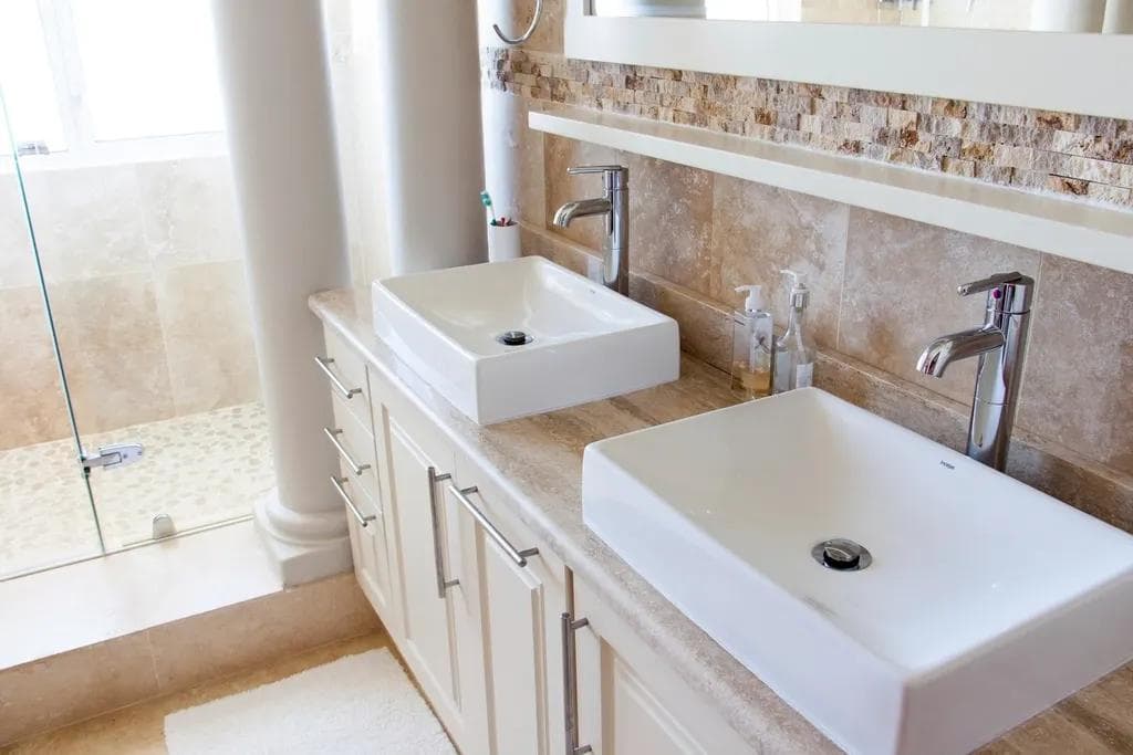 Two white countertop wash basins with chrome taps on a bathroom vanity