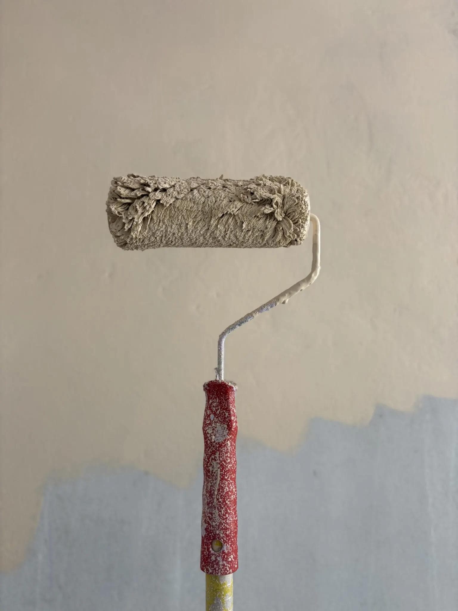 Paint roller held against a partly painted wall